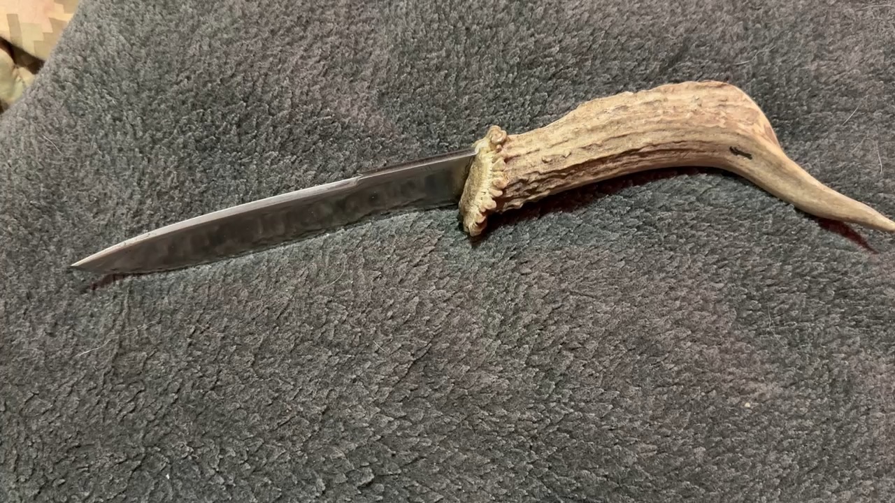 Finished narrow knife with a natural antler handle on a dark surface