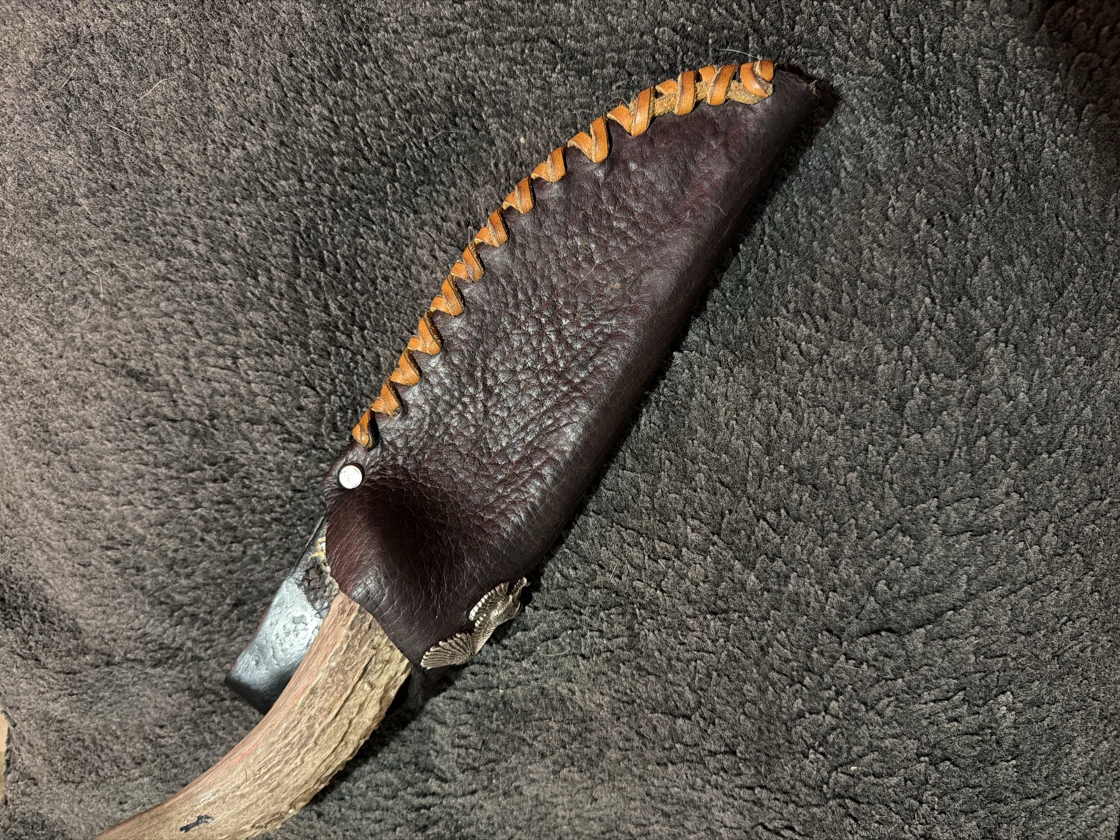 Antler-handled knife partially seated in a hand-laced brown leather sheath