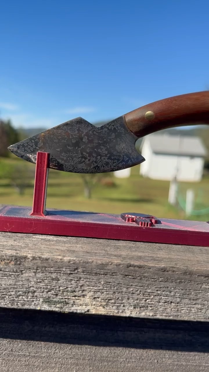 Compact forged knife with a wood handle displayed outdoors on a red stand