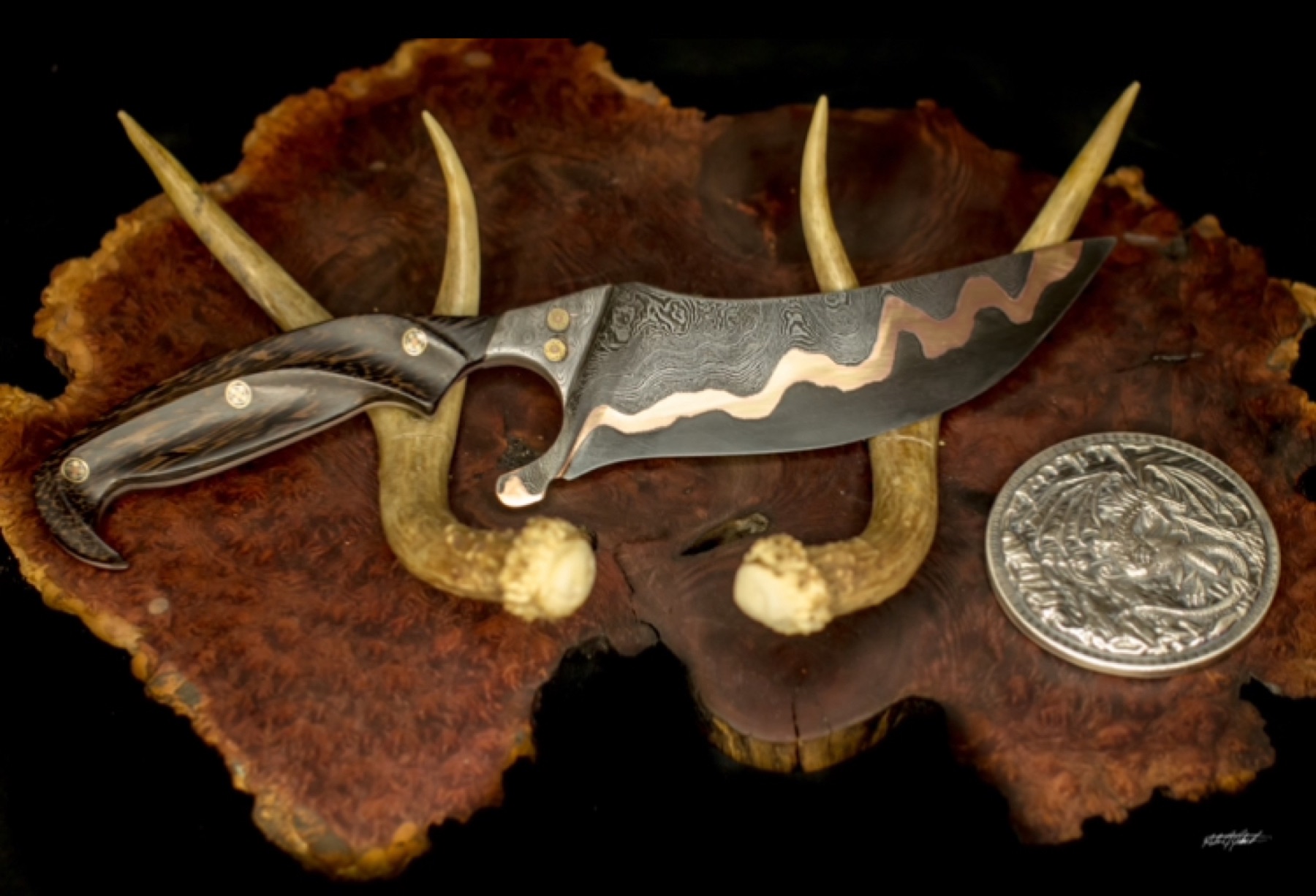 Copper-inlay custom knife displayed on burl wood with antlers and a wolf medallion