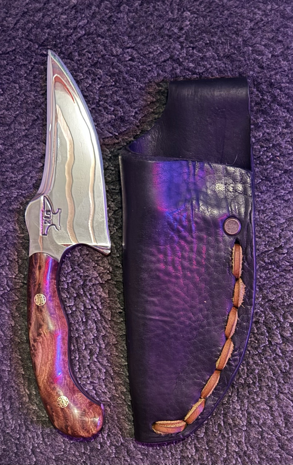 Copper-inlay Tulos knife beside its black leather sheath under purple studio light