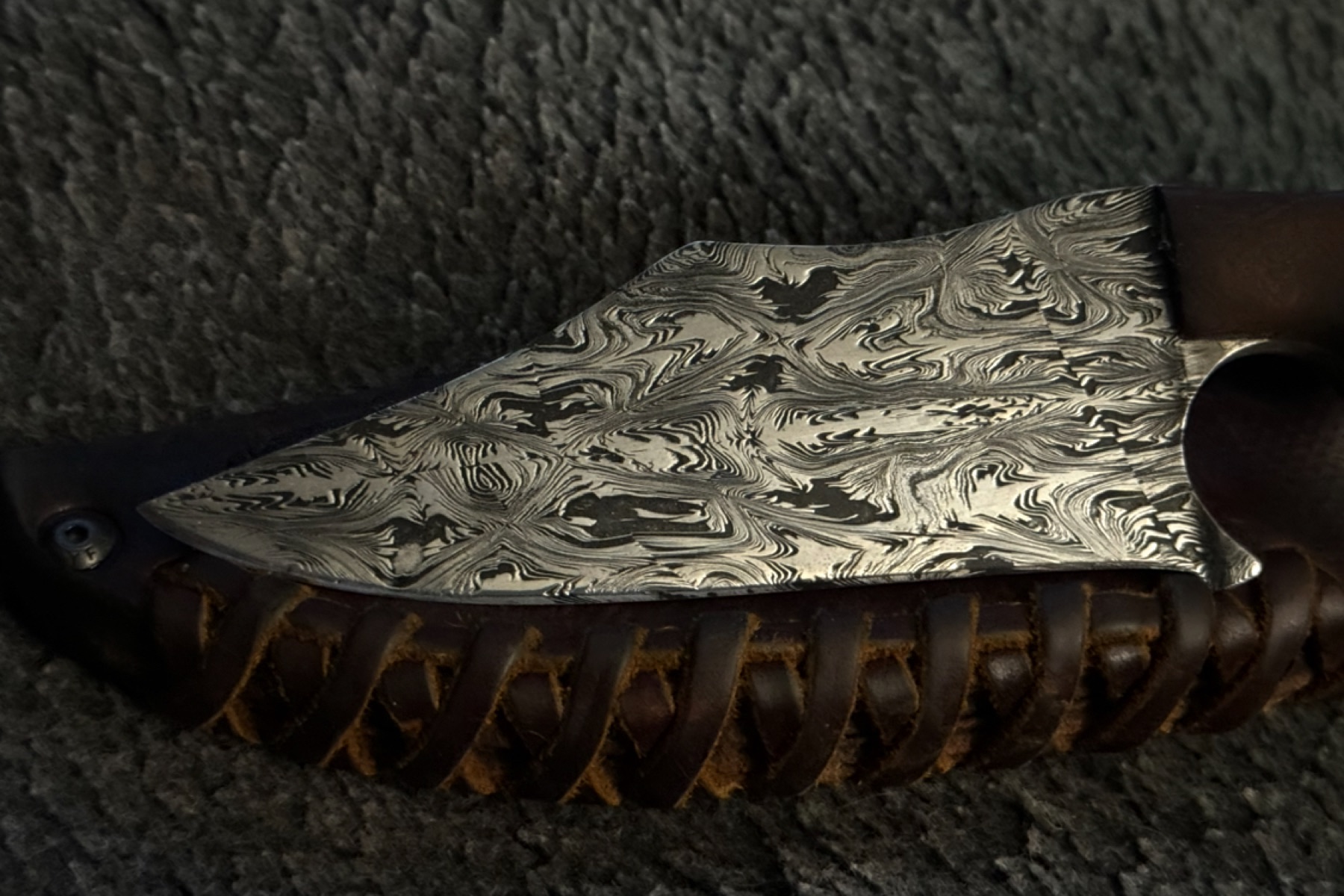 Pattern-welded Damascus Tulos blade resting in a hand-laced brown leather sheath