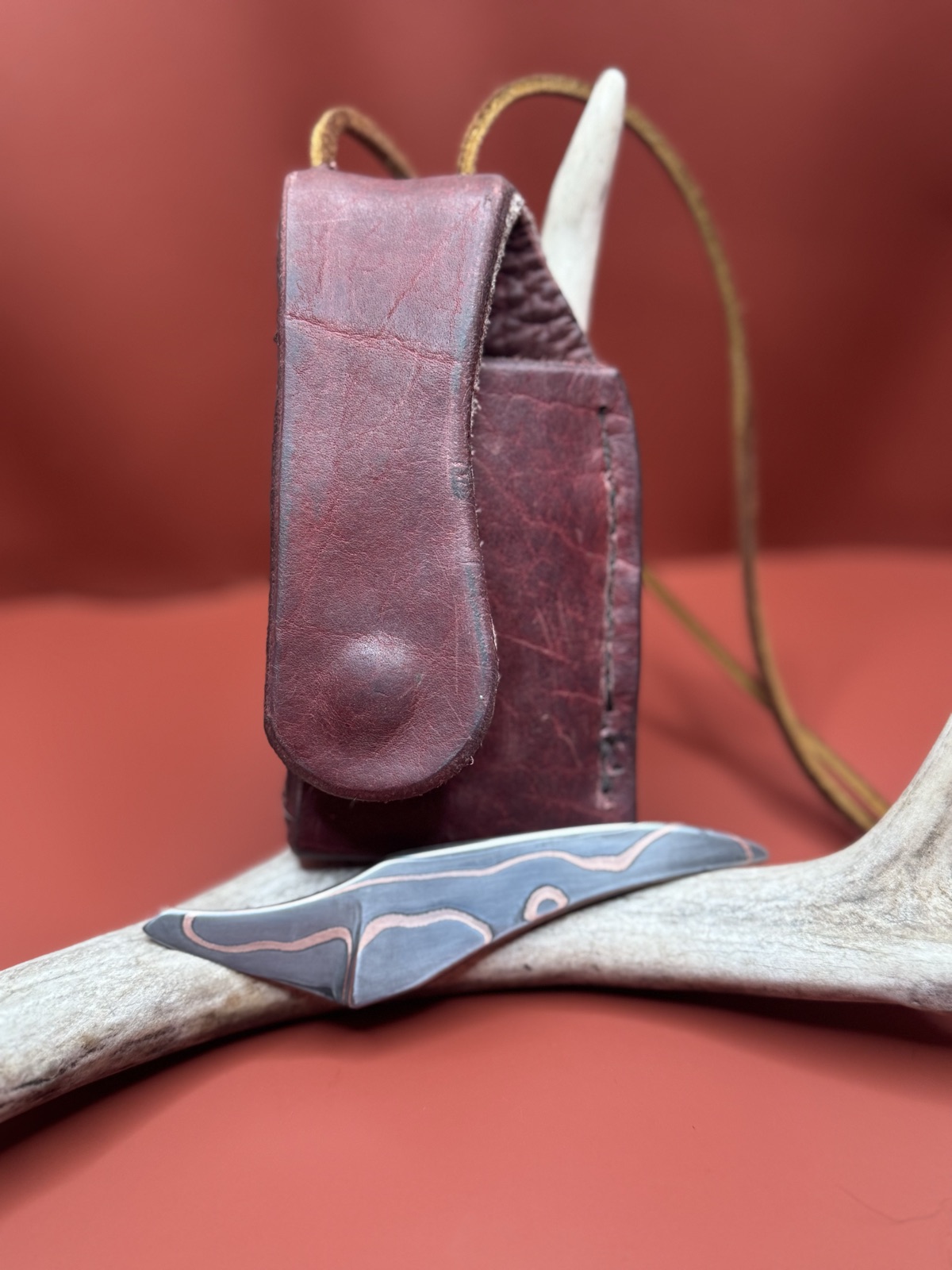 Small copper-inlay Tulos knife displayed with a fitted burgundy leather sheath