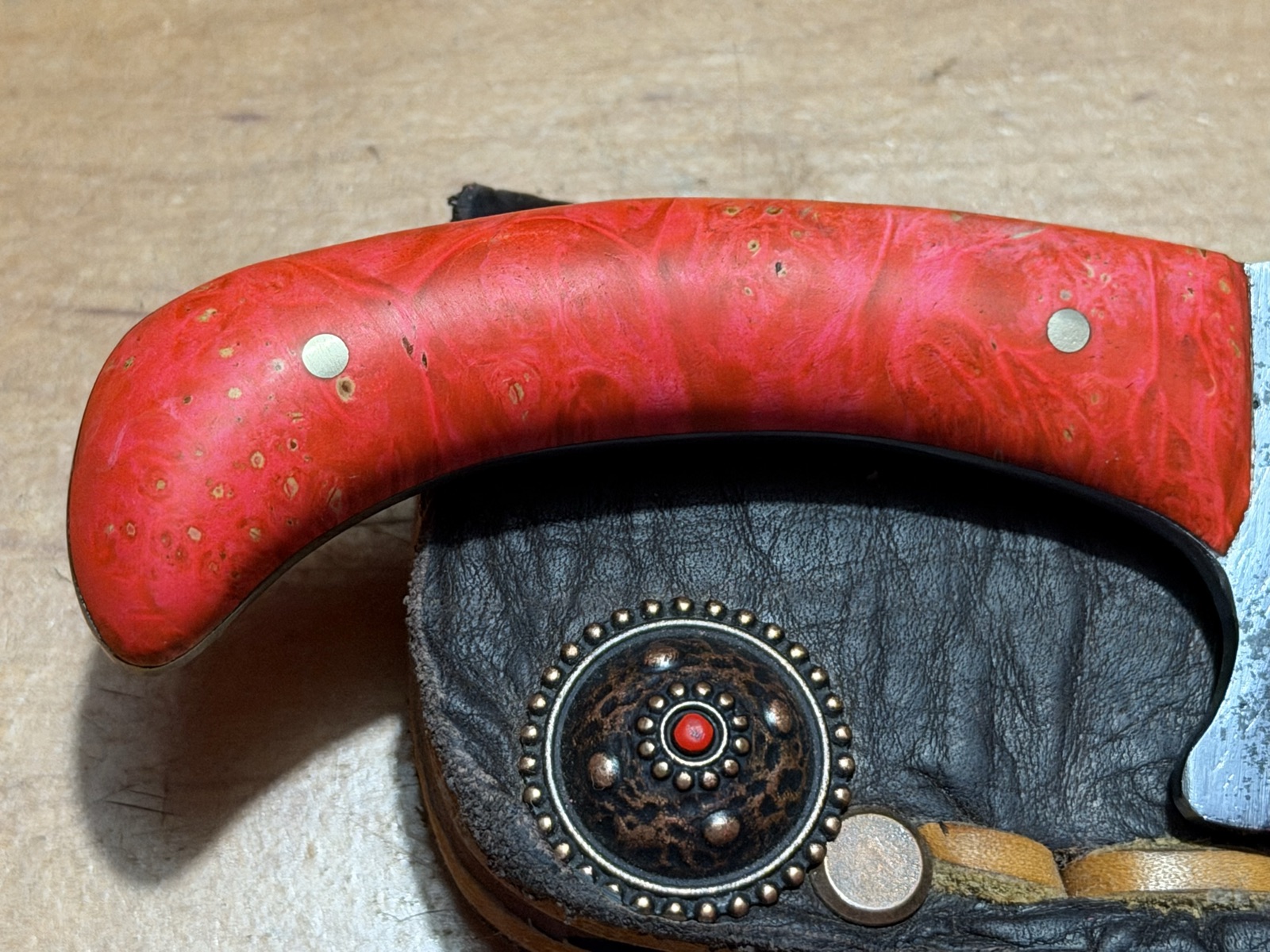 Close detail of a decorative button and stitching on a black Tulos leather sheath