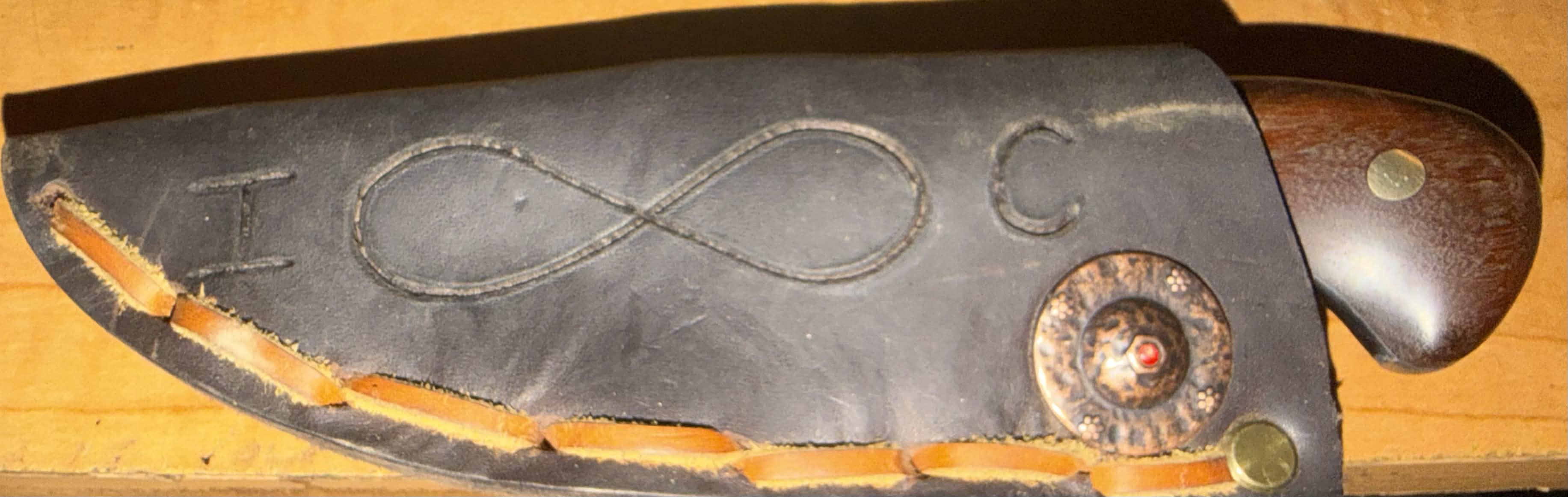 Black leather knife sheath with an infinity symbol and detailed copper-toned hardware