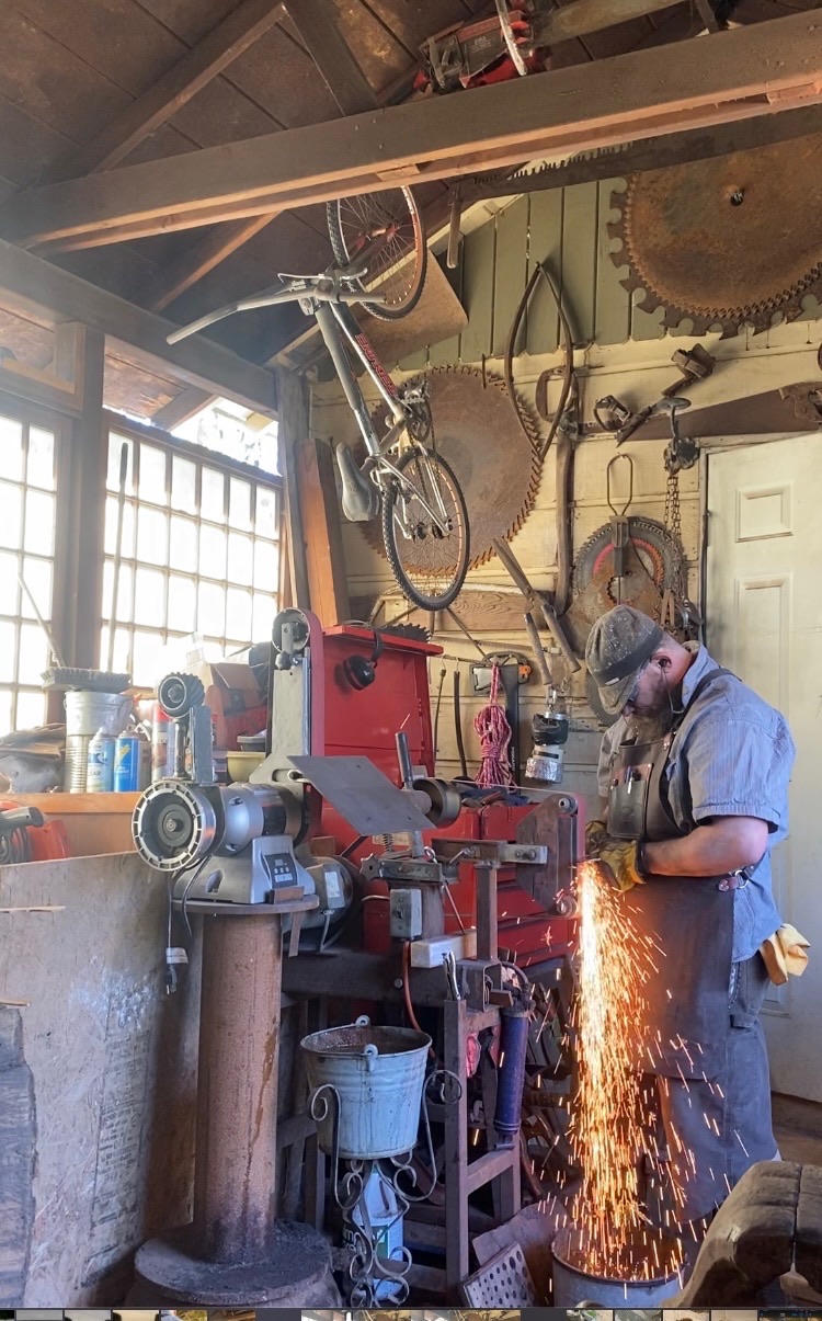 Tulos grinding steel in a crowded workshop as sparks fall toward the floor